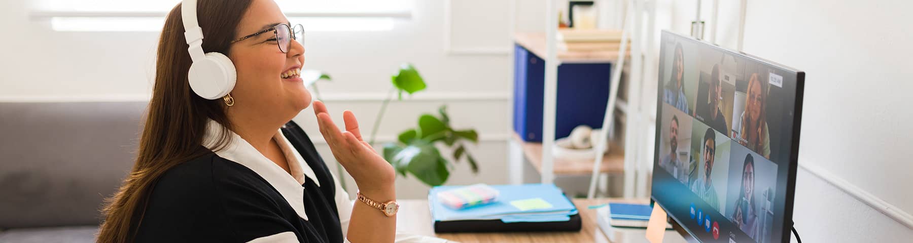 Woman wearing headphones smiling during a video call at her desk.