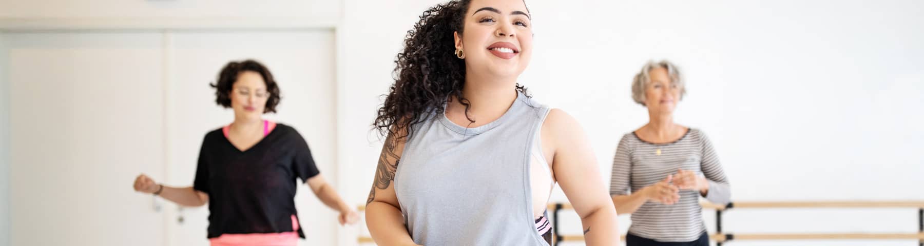 Smiling young woman in a fitness class, dancing with two other participants in the background.