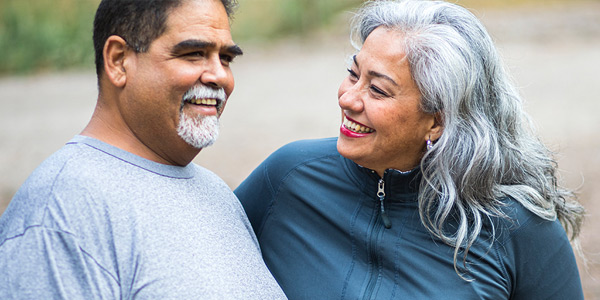 Smiling middle-aged man and woman standing outdoors and looking at each other.