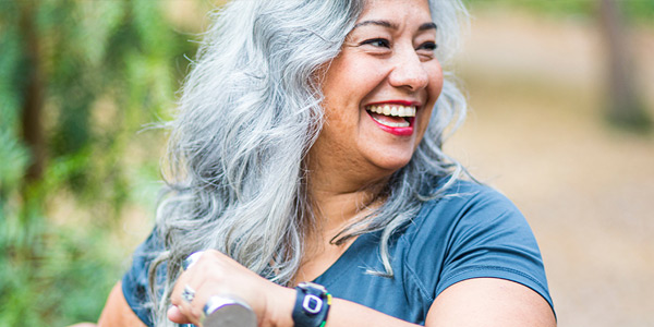 Smiling middle-aged woman with gray hair holding a dumbbell outdoors.