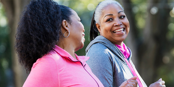 Two women smiling and walking outdoors in athletic wear.